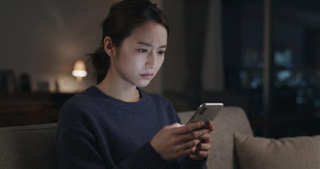 元彼への連絡を迷い、スマートフォンを手にしながら考え込む女性。焦って行動したくなる気持ち
メッセージを送るか迷っている様子